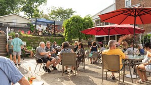 An outdoor patio with tables and chairs, a stage with people, and a brick building in the background. - Charming Apartment in the heart of Downtown LeClaire sleeps 4 (Le Claire)