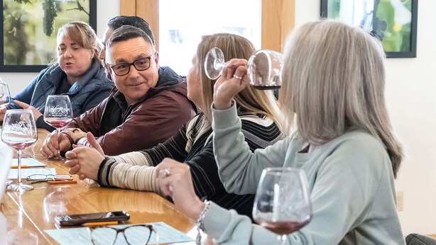 A group of people seated around a wooden table with wine glasses, engaged in a discussion. - Charming Apartment in the heart of Downtown LeClaire sleeps 4 (Le Claire)