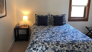 A bedroom with a bed, a bedside table with a lamp, a window, and a framed picture on the wall. - Charming Apartment in the heart of Downtown LeClaire sleeps 4 (Le Claire)