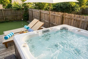 Ein Whirlpool auf einer Holzterrasse mit Liegestühlen und einem Sonnenschirm.