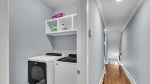 A laundry room with a washing machine and dryer, a shelf with cleaning supplies, and a wooden floor. - Nashville sleeps 24: 2 homes, hot tub & game room near broadway (Nashville)