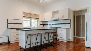 Una cocina moderna con una isla central, taburetes de bar, armarios blancos y un ventanal con persianas.