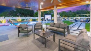 An outdoor patio area with a pool, seating, and a stage. - Athletic Villa Football Field Gym Cinema (North Miami)