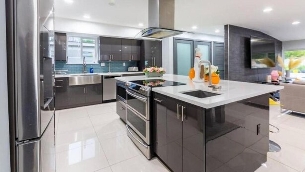 A modern kitchen with stainless steel appliances, a central island, and dark cabinetry. - Athletic Villa Football Field Gym Cinema (North Miami)