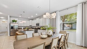 Een moderne keuken met witte kastjes, een centraal eiland en een eethoek met een houten tafel en stoelen.