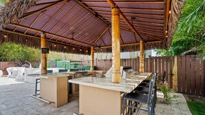 Un espace cuisine extérieur doté d’une pergola, d’un coin barbecue et de différents espaces pour s’asseoir.