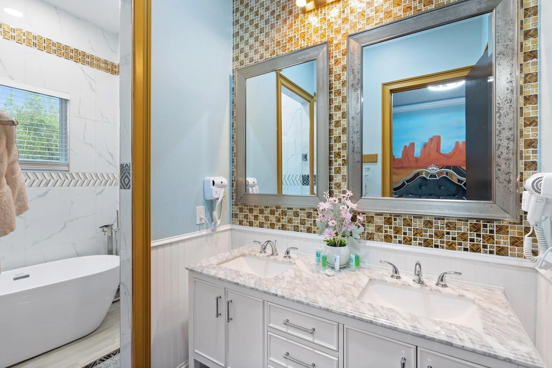 Ein Badezimmer mit einer Badewanne, zwei Waschbecken, einem Schminktisch mit Schubladen, einem großen Spiegel und einem Fenster mit Blick auf Grünflächen.