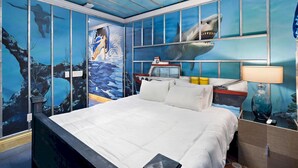 Une chambre à coucher comprenant un lit, une table de chevet, une lampe et des murs décorés de fresques représentant la vie marine.