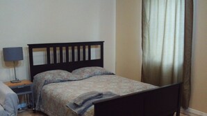 A bedroom with a bed, a nightstand with a lamp, and a window with curtains. - Peaceful studio with AC in charming Laguna Hills (Laguna Hills)