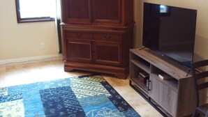 A room with a large wooden cabinet, a flat-screen TV on a stand, and a patterned rug. - Peaceful studio with AC in charming Laguna Hills (Laguna Hills)