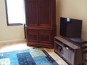 Una habitación con un gran armario de madera, un televisor de pantalla plana sobre un soporte y una alfombra estampada.