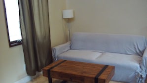 A living room with a sofa, a wooden coffee table, a lamp, and a window with curtains. - Peaceful studio with AC in charming Laguna Hills (Laguna Hills)