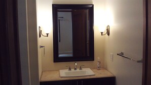 A bathroom with a white sink, dark cabinets, and a large mirror. There are wall sconces on either side of the mirror. - Peaceful studio with AC in charming Laguna Hills (Laguna Hills)