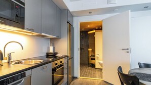 Une cuisine compacte dotée d’appareils électroménagers modernes, un coin repas avec une table et des chaises, et une salle de bain visible avec une douche.