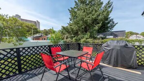 A deck with a table and chairs, a barbecue grill, and a view of trees and buildings. - Last minute and Fall specials! Walk to beach! 4br 4ba Perfect location  (North Myrtle Beach)