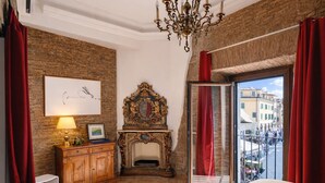 A bedroom with a fireplace, a chandelier, a view of the street, and a wooden cabinet. - La Torre del Biscone   Campo dè Fiori (ROMA)