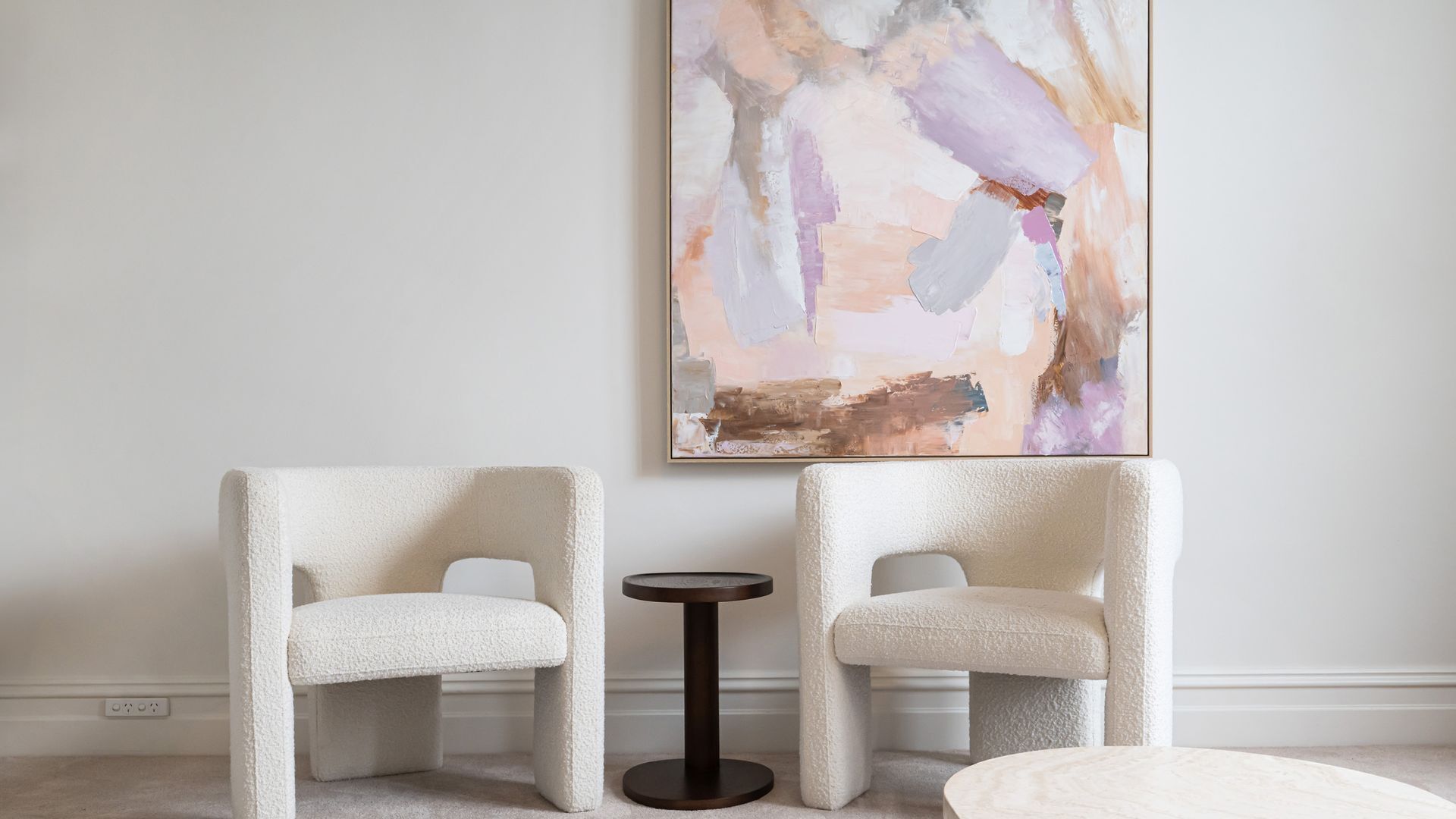 A room with two white armchairs, a small round table, and a large abstract painting on the wall.