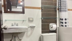 Une salle de bain comprenant des toilettes, un lavabo, une étagère en verre et un rideau de douche.