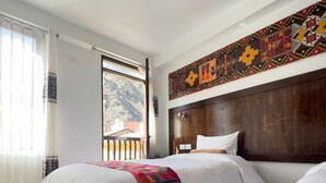 Ett hotellrum med två sängar, en sänggavel i trä, ett stort fönster med gardiner och en färgstark väggdekoration.