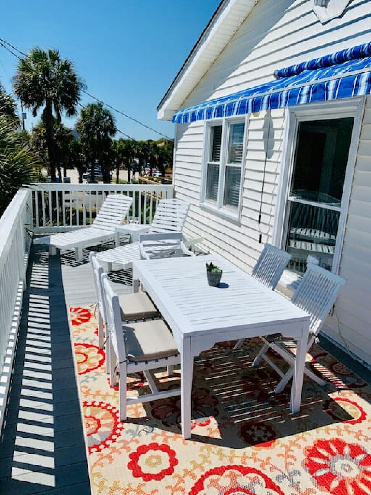 Une maison blanche avec un porche couvert, des meubles blancs et un tapis à motifs.