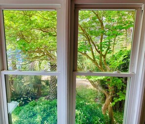 A window with a view of a lush garden with various trees and plants. - Sea Spot - Up! Beach access/Deck/Ocean view (Folly Beach)