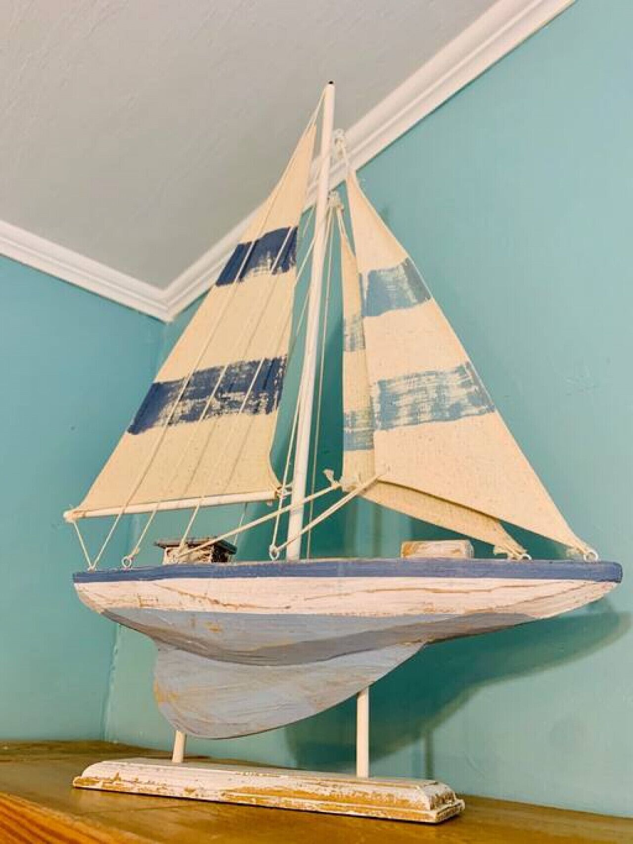 Een model zeilboot op een houten basis, voor een blauwgroene muur.