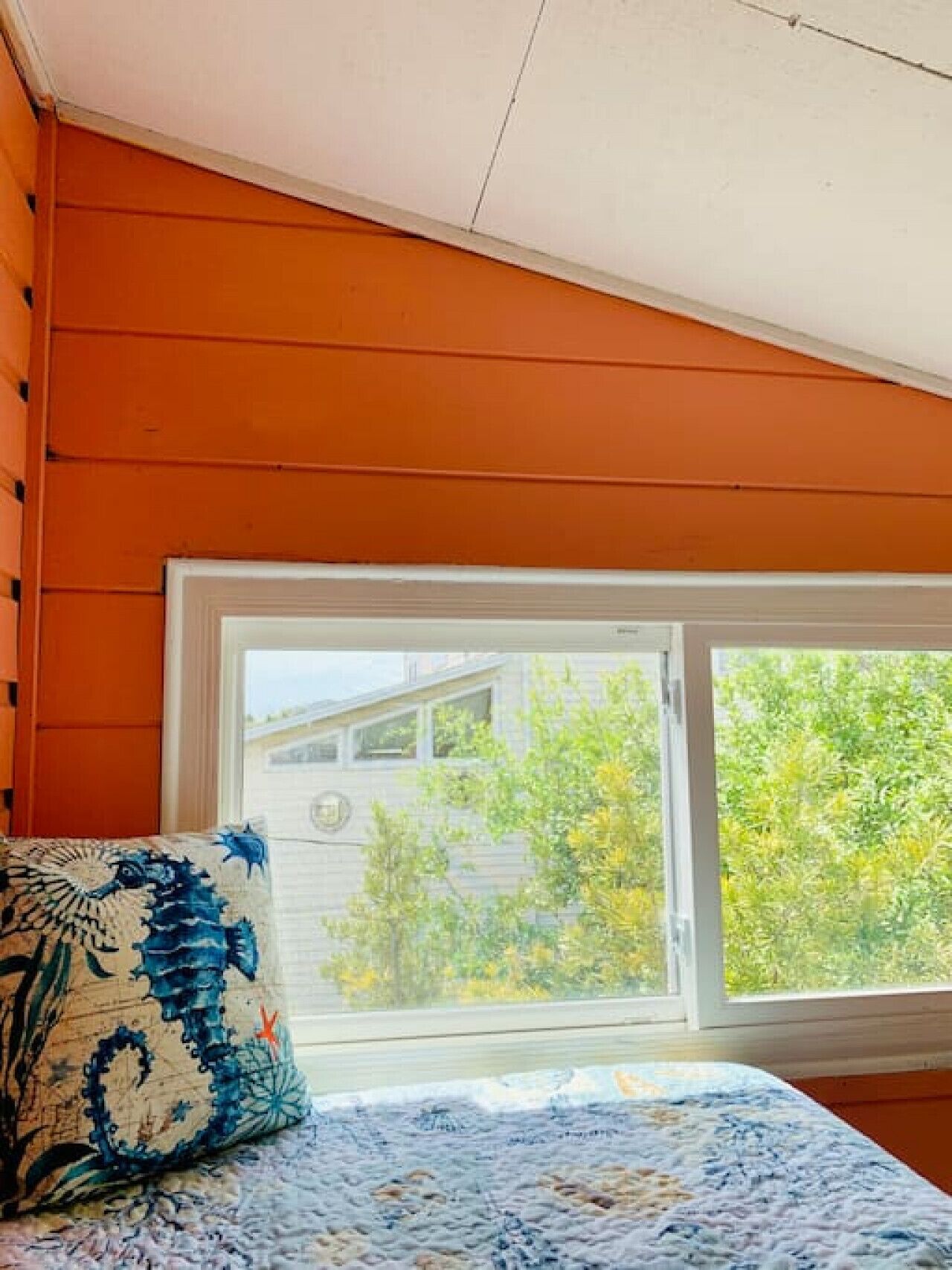 A room with a bed, a window, and a view of a house and trees.