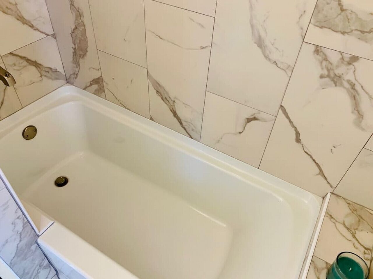 Une salle de bain avec une baignoire blanche, des carreaux de marbre et une bouteille verte posée sur le sol.