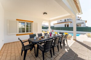 Une terrasse extérieure avec une table dressée pour le repas, entourée de chaises, et une piscine en arrière-plan.