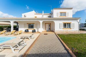 Un bâtiment blanc à deux étages, doté d’un toit en tuiles, d’une piscine et de chaises longues.