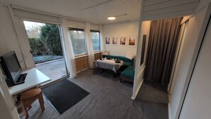 A compact room with a desk, a green sofa, a small table, and a TV. - Vacation home with large terrace in Schöneiche near Berlin (Schöneiche bei Berlin)