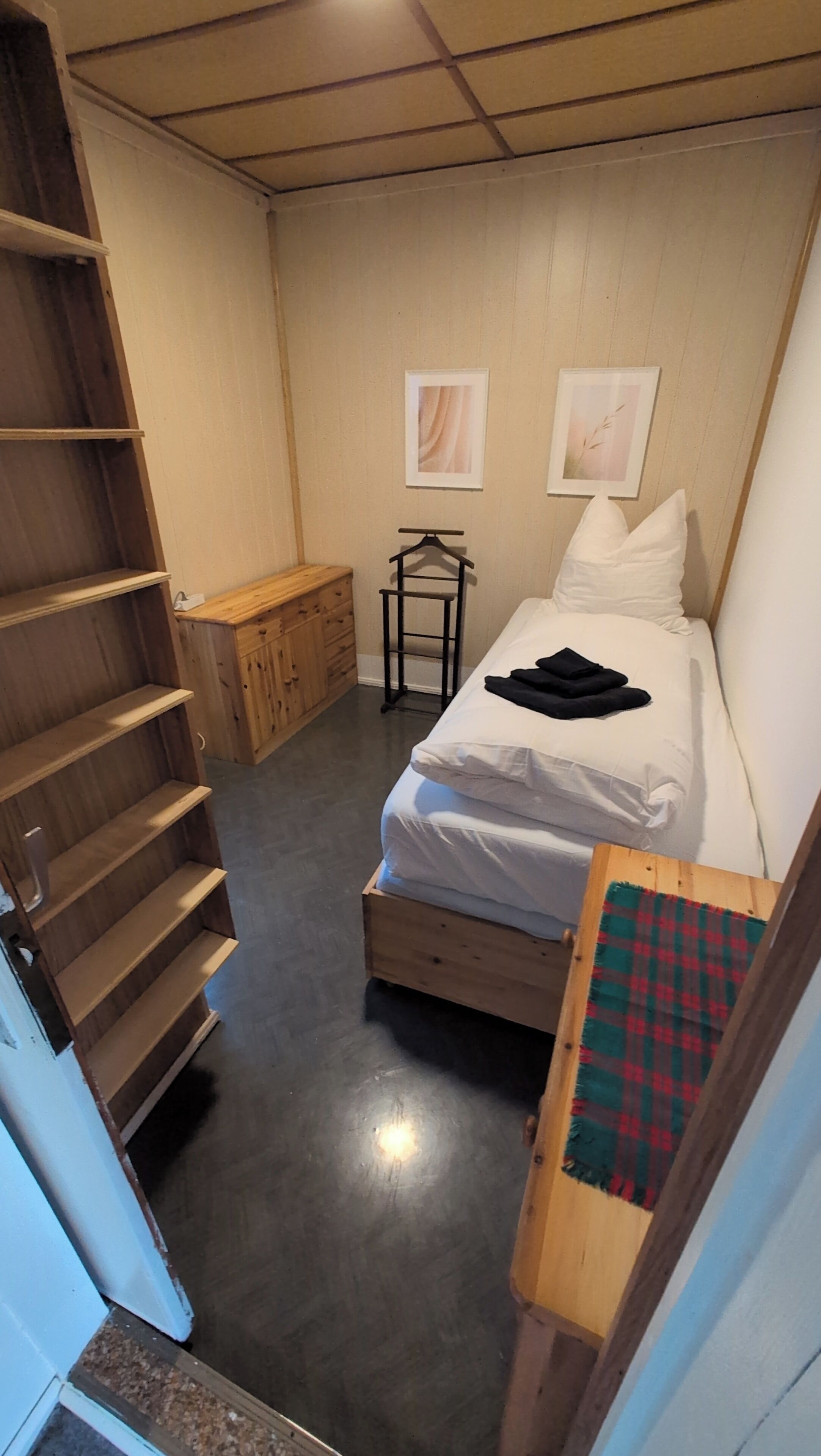 A bedroom with a bed, a wooden dresser, a small table, and a staircase.