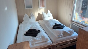 A small, compact room with two single beds, a wooden bench, a window with a view of the outside, and a ceiling with a grid pattern. - Vacation home with large terrace in Schöneiche near Berlin (Schöneiche bei Berlin)