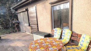 An outdoor seating area with a round table covered by a floral tablecloth, two wooden chairs with floral cushions, and a small table with a speaker. - Vacation home with large terrace in Schöneiche near Berlin (Schöneiche bei Berlin)