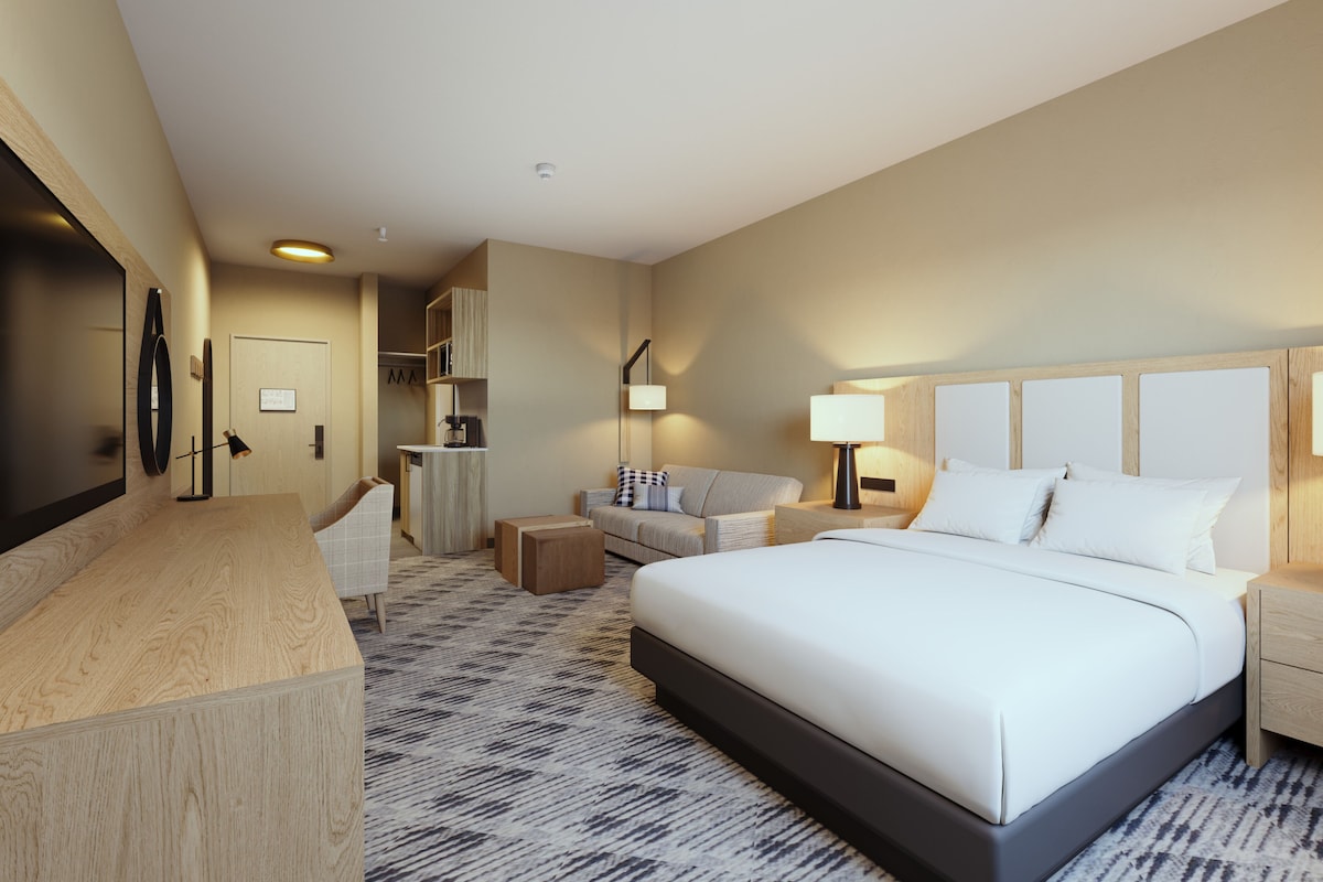 Habitación de hotel con una cama grande, un escritorio, una silla, un sofá y una pequeña kitchenette.