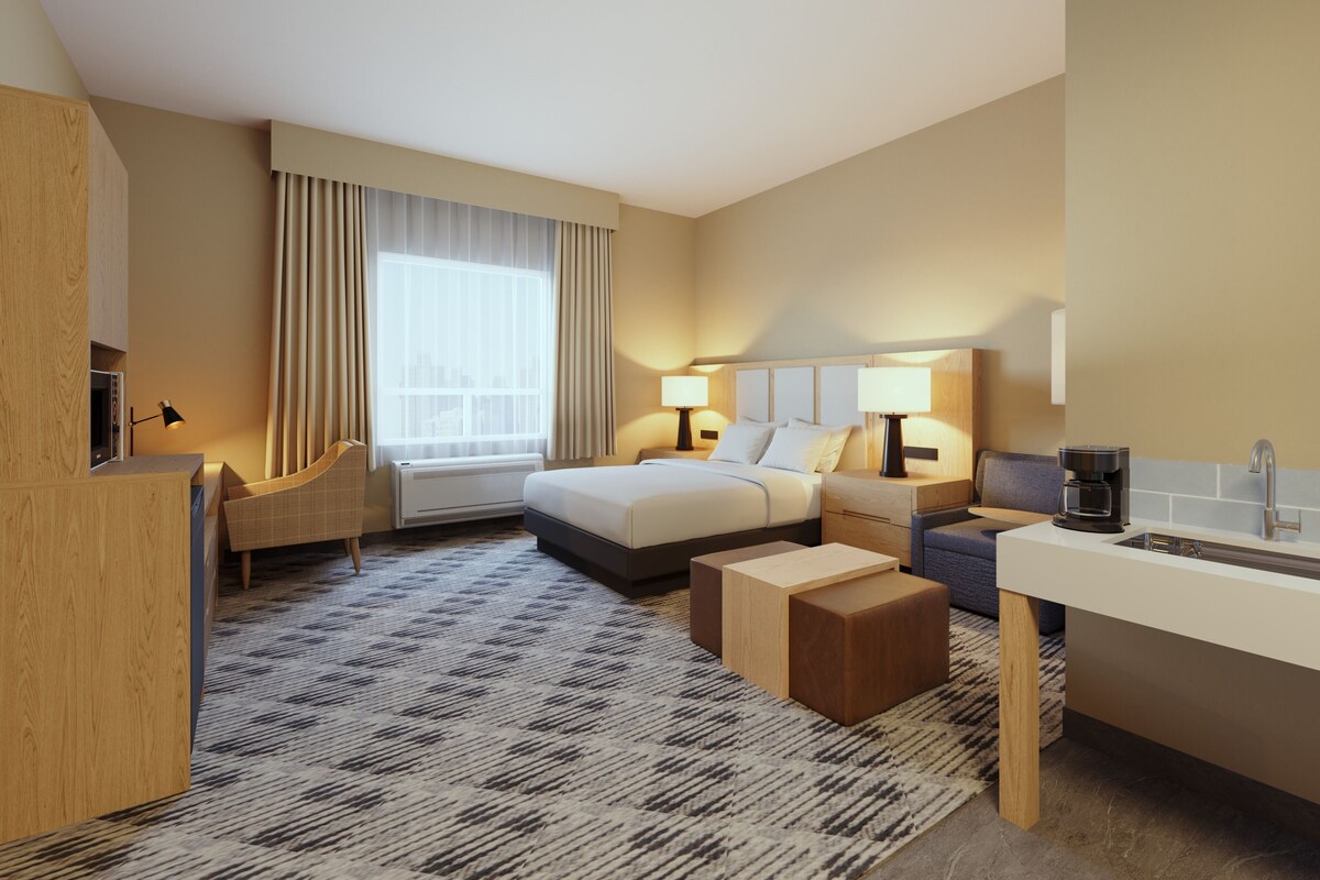 Habitación de hotel con cama, mesitas de noche, escritorio, silla, sofá, cafetera y ventana con cortinas.
