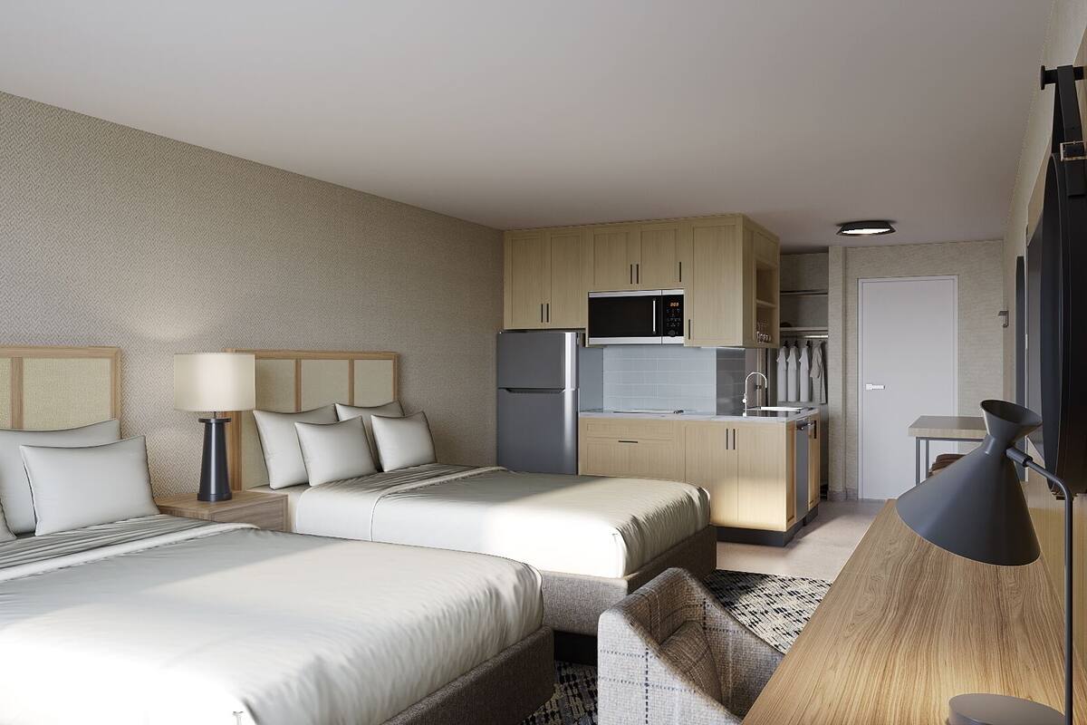 Ett hotellrum med två sängar, ett litet kök, ett skrivbord och en stol.
