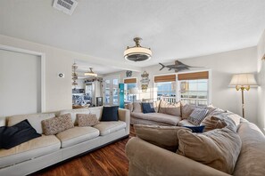 A spacious living room with two beige sofas, a wooden floor, and a large window with a view. - Cozy Cottage - Dog friendly, Near the Beach! (Galveston)