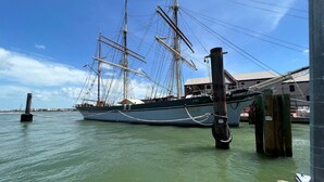 Ein großes Segelschiff liegt in einer Marina vor Anker, der Himmel ist wolkenlos und das Wasser ruhig.