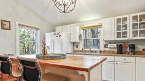 Une cuisine moderne avec des meubles blancs, un îlot central en bois, des tabourets de bar et un lustre.