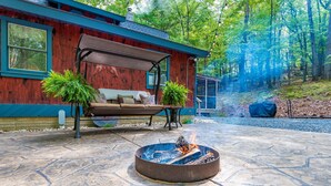 Une terrasse avec un foyer, une plateforme en bois et une maison bleue dotée d’un espace salon abrité.