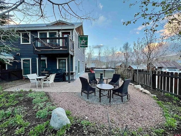 Ein zweistöckiges Haus mit Balkon, Sitzbereich im Freien mit Stühlen und Tischen sowie einer gepflasterten Terrasse.