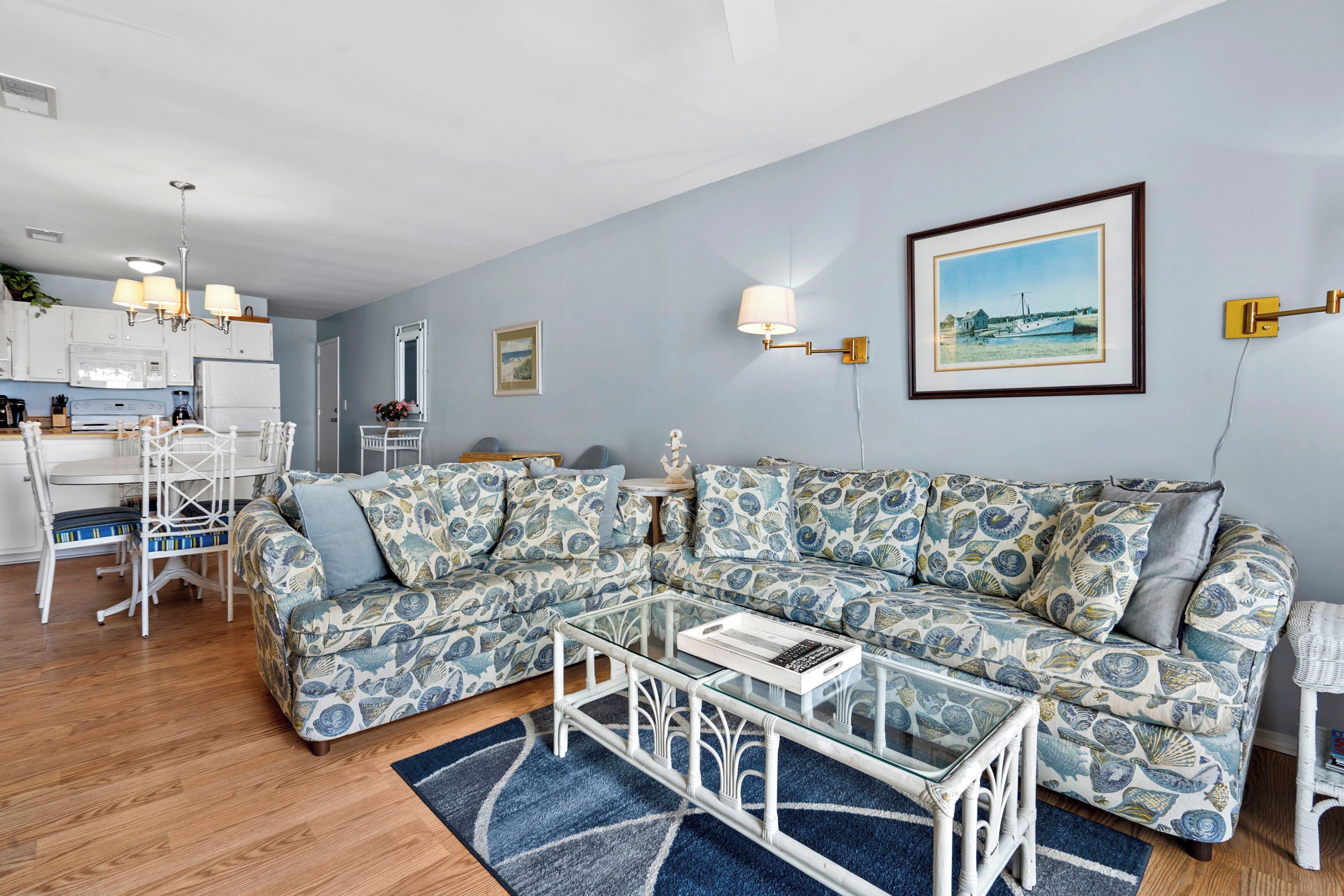 A living room with a sectional sofa, a glass coffee table, and a dining area with a white table and chairs.