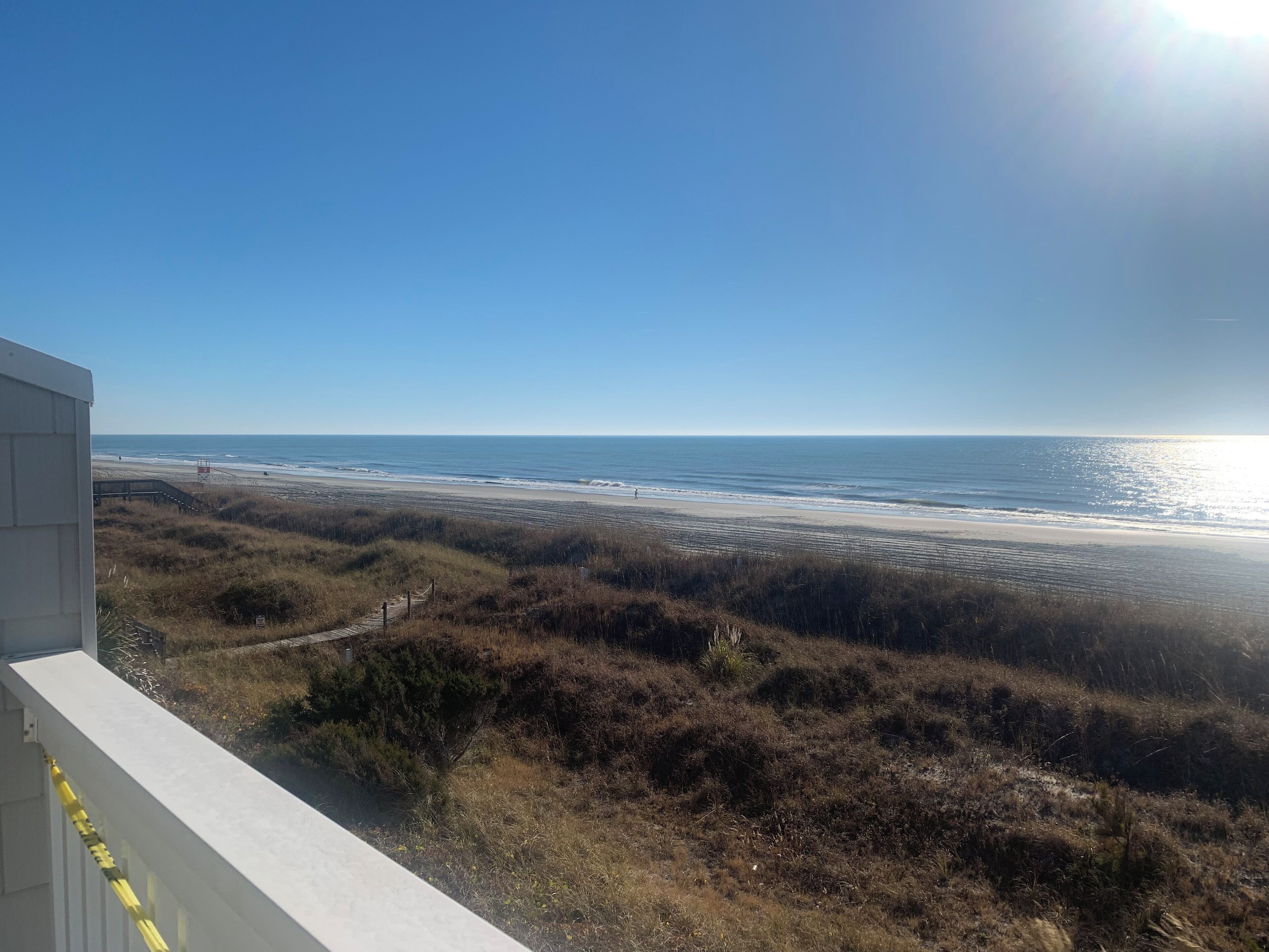 A coastal view from a balcony overlooking a beach with a clear sky.