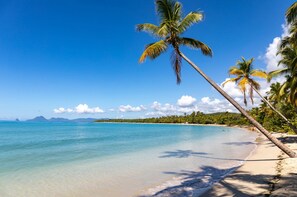 Ein Strand mit klarem türkisblauem Wasser, Palmen und einer fernen Bergkette.
