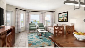 A modern living room with a TV, green armchairs, a white sofa, a wooden dining table, and a view of the ocean. - Ocean View/Ocean Side  2BR at Aruba Surf Club – Steps to Palm Beach Paradise (Noord)