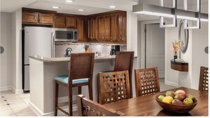 A kitchen with wooden cabinets, a central island with seating, a dining table with chairs, and a fruit bowl. - Ocean View/Ocean Side  2BR at Aruba Surf Club – Steps to Palm Beach Paradise (Noord)