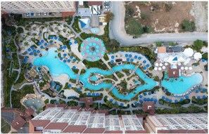 Vista aérea de um resort com várias piscinas, áreas de estar e um estacionamento.