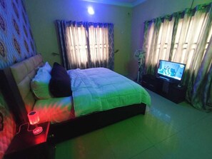Ein Schlafzimmer mit einem Bett, einem Fernseher, Vorhängen und einem Ventilator.