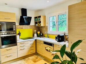 A modern kitchen with built-in appliances, a window with a view, and a plant. - Villa NAHEMA – Private Pool, 2 Minutes from Port Grimaud Gulf of Saint-Tropez (Grimaud)